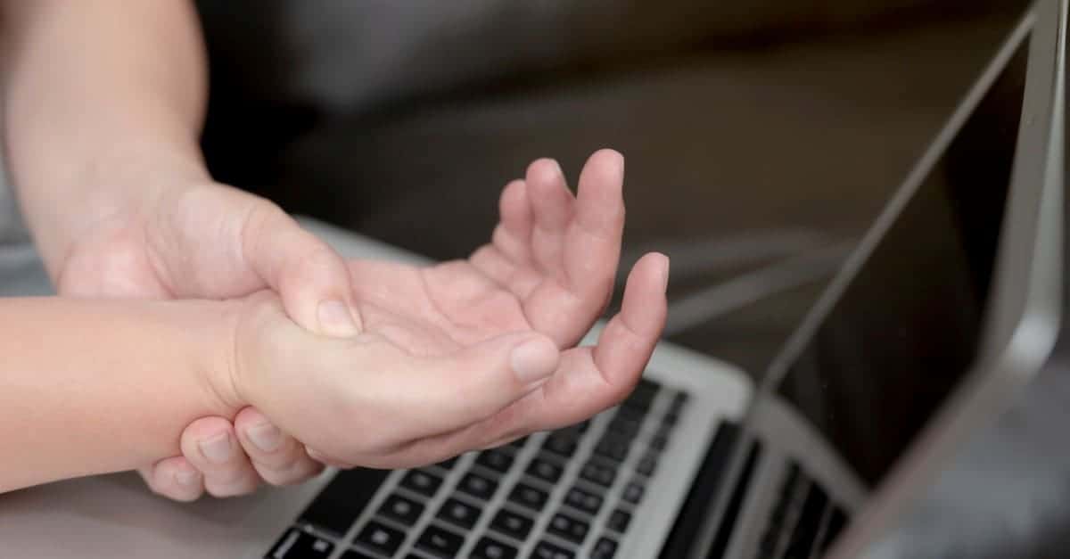 Person sitting in front of a computer and experiencing hand numbness and pain