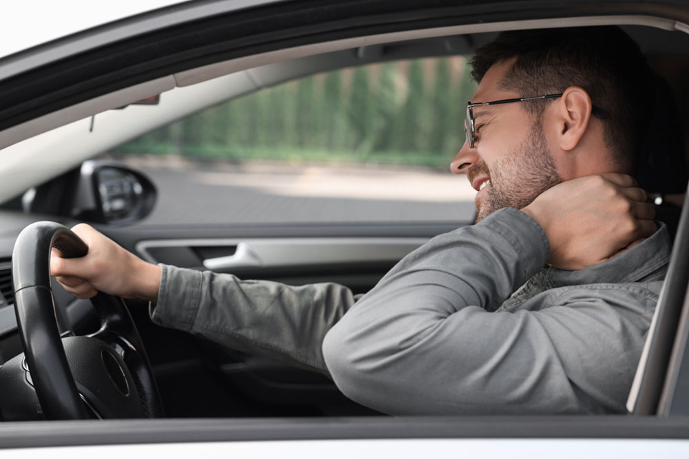 a man is sitting in a car after a car accident rubbbing his neck after a whiplash